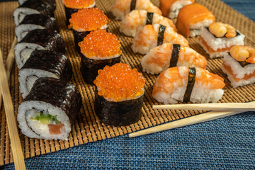 Sushi and rolls with red caviar and shrimp on a bamboo mat with food sticks