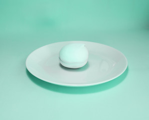 One pastel soft marshmallow on a turquoise plate. Total biscay green background.