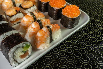 Sushi and rolls with red caviar and shrimp on a white dish