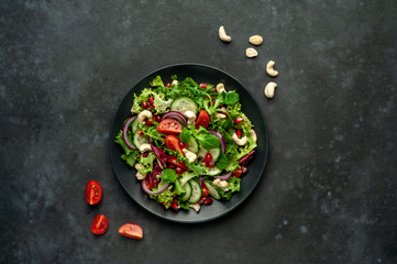Salad with pomegranate, tomatoes, fresh cucumbers, onions, sesame seeds and cashew nuts, spices on a stone background. Healthy vegetarian food.