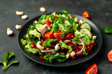 Salad with pomegranate, tomatoes, fresh cucumbers, onions, sesame seeds and cashew nuts, spices on a stone background. Healthy vegetarian food.