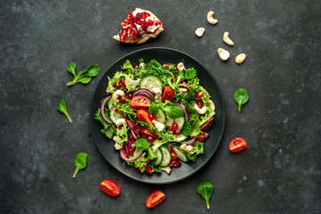 Salad with pomegranate, tomatoes, fresh cucumbers, onions, sesame seeds and cashew nuts, spices on a stone background. Healthy vegetarian food.