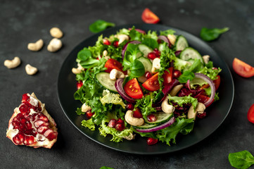 Salad with pomegranate, tomatoes, fresh cucumbers, onions, sesame seeds and cashew nuts, spices on a stone background. Healthy vegetarian food.