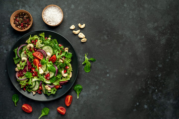 Obraz na płótnie Canvas Salad with pomegranate, tomatoes, fresh cucumbers, onions, sesame seeds and cashew nuts, spices on a stone background. Healthy vegetarian food. with copy space for your text