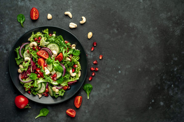 Salad with pomegranate, tomatoes, fresh cucumbers, onions, sesame seeds and cashew nuts, spices on a stone background. Healthy vegetarian food. with copy space for your text