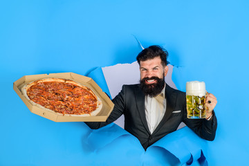 Pizza delivery concept. Bearded man with tasty pizza and beer looking through paper hole. Pizza time. Fastfood. Italian food. Satisfied man with beard and mustache enjoy delicious pizza and cold beer.