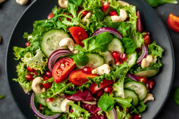 Salad with pomegranate, tomatoes, fresh cucumbers, onions, sesame seeds and cashew nuts, spices on a stone background. Healthy vegetarian food.