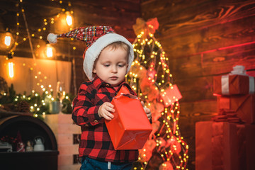 Fototapeta na wymiar Little baby with Christmas gift in his hands on the Christmas background. Small kid with Santa hat. Merry Christmas and happy holidays.
