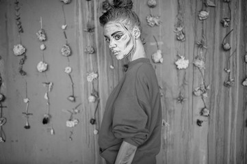 Young girl with creative body art standing against decorative wallpaper with dried flowers.