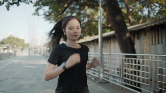 Medium shot. Asian female runner wear black athletic sportswear suit  running on bridge a walkway in the city