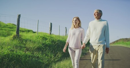 Happy senior couple smiling and enjoying a walk outdoors together holding hands, older couple enjoying their retirement years and living healthy - Powered by Adobe