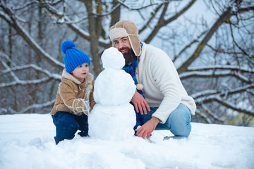 Fototapeta na wymiar Father and son making snowman. Winter background with snowflakes and snowman. Merry Christmas and Happy new year. Happy loving family. Father and son playing with snow in park on white snow background