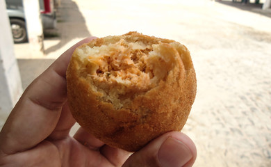Holding a COXINHA DE FRANGO and having blue sky with cloud as background. The COXINHA DE FRANGO is a very popular food in Brazil.