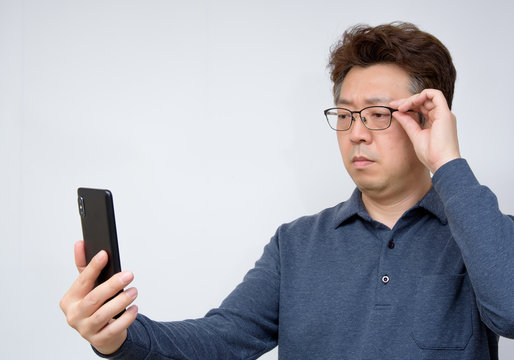 Asian Male Trying To Read Something On His Mobile Phone. Poor Sight, Presbyopia, Myopia.