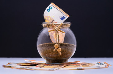 Travel money savings in a jar filled with sand and decorated with a starfish. Euro cash money notes.  Holiday concept isolated on gradient black background.