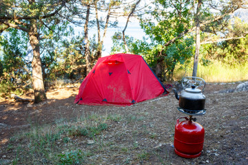 Cooking camping kettle on a red gas bottle. Tent and sea background