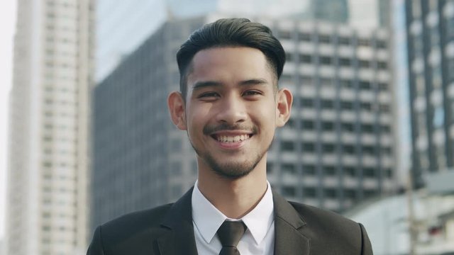  Medium close up. Portrait of Handsome young businessman standing outside the office and smiling happily On the background of city building