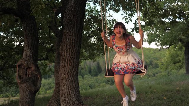 child swinging on a swing in park in sun. teen girl enjoys flight on swing on summer evening in forest. concept of happy family and childhood.