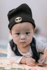 Asian baby boy wearing black knitted beanie lying on play mat during tummy time at home