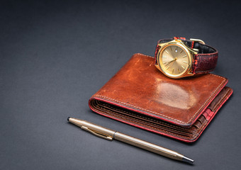 Brown leather wallet with watch and gold pen isolated on black gradient background. Luxury accessories. Gift concept for men. 