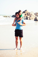 happy family on beach playing, father with son walking sea coast, rocks behind smiling taking vacation