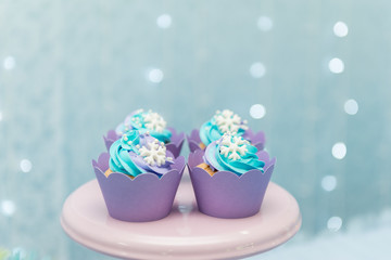 Set of tasty cupcakes with blue and purple cream icing on a pink tray on blue background and defocused lights. Selective focus. Pastel colors. Party concept. Children's party decoration.