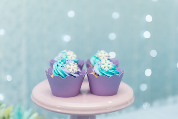 Set of tasty cupcakes with blue and purple cream icing on a pink tray on blue background and defocused lights. Selective focus. Pastel colors. Party concept. Children's party decoration.