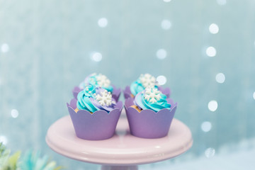 Set of tasty cupcakes with blue and purple cream icing on a pink tray on blue background and defocused lights. Selective focus. Pastel colors. Party concept. Children's party decoration.