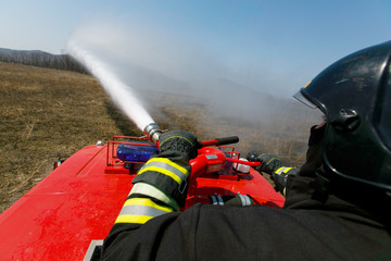 Close-up. A firefighter puts out a hot field with a water cannon.