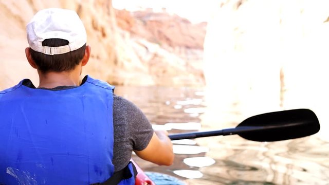 Back of man swimming kayaking motion fast in Lake Powell water antelope canyon with paddle oar and life jacket vest