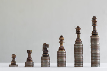 Coin stacks arranged with chess pieces into growth chart on white background, finance and business...
