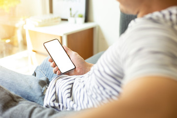 Mockup image blank white screen cell phone.men hand holding texting using mobile on sofa at home office. background empty space for advertise text.people contact marketing business and technology 