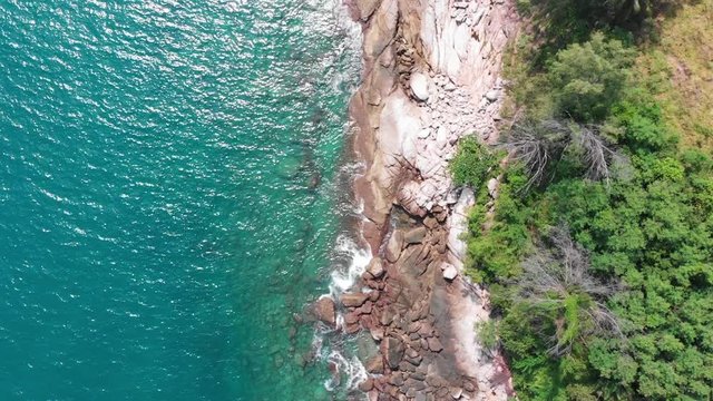 Aerial Top Down View Over Turquoise Waters Gently Crashing Onto Rocky Coastline In Nai Harn, Phuket, Thailand. Slow Motion