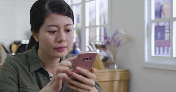 slow motion charming asian chinese woman reading news on mobile phone during rest in morning at home. young girl using cellphone browsing online website in modern wooden kitchen in free time alone.