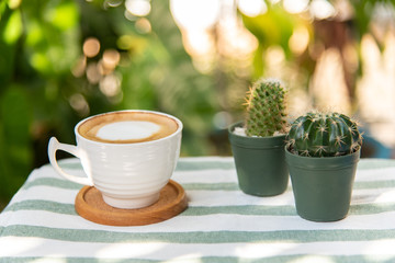 Hot latte cup and cactus pots on a white-green striped fabric 
