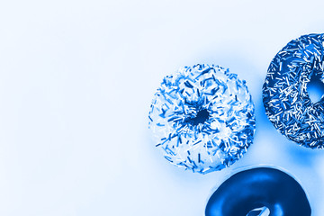Three tasty doughnuts on blue background. Trendy 2020 color concept.