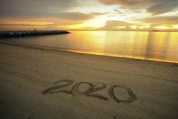 Fototapeta premium Welcoming new year concept. Welcome 2020 written on sandy beach with beautiful sunset background.
