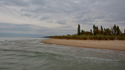 Fototapeta na wymiar Photo of a sandy Lake Michigan beach and shoreline on a cloudy day with small waves and surf 