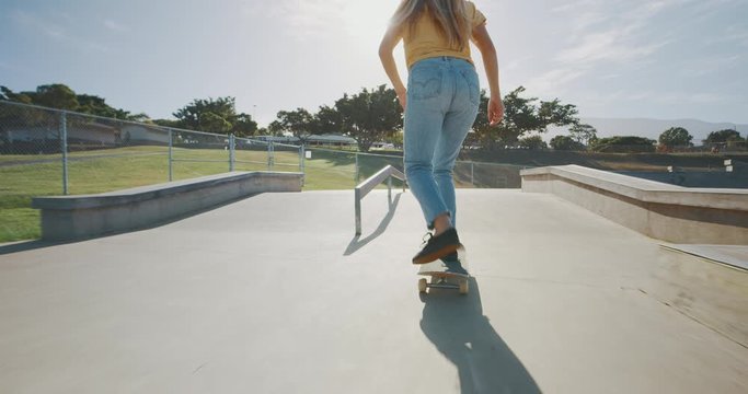 Stylish girl skateboarding in a skatepark at sunrise backlit, tracking shot of a girls legs riding a skateboard