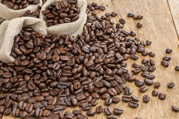 Roasted coffee beans and coffee bean bags placed on a wooden table, top view.