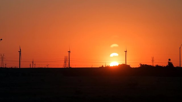 Snyder, USA view of wind turbine farm and power lines in Texas countryside industrial town and horizon with timelapse of colorful red sunrise 
