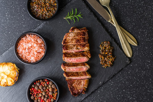 New York Strip Loin Beef Steak Meat With Chimichurri Sauce Against Black Stone Background