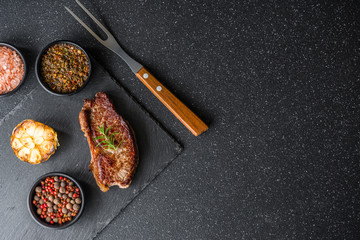 New york strip loin beef steak meat with chimichurri sauce against black stone background