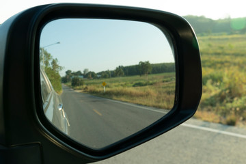 Car's side view mirror. On a rural road area with pastures.