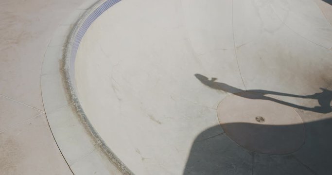 Stylish skater girl skateboarding doing a big carve around the top of a concrete bowl in slow motion, old vintage filmy look skateboarding girl