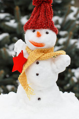 Decorated snowman with woolen scarf and cap, background of coniferous tree covered snow