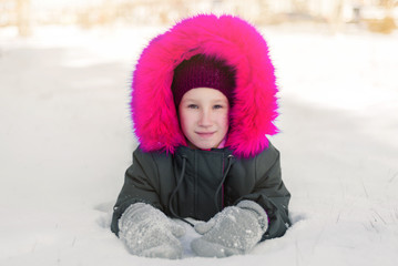 little girl child lying on the snow in a hat and mittens in winter in the Park
