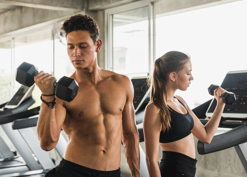 Fitness man and woman holding dumbbell standing posing near treadmill. Muscular couple training at the gym.