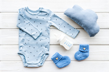 Blue bodysuit for baby boy near children's accessories on white wooden background top-down