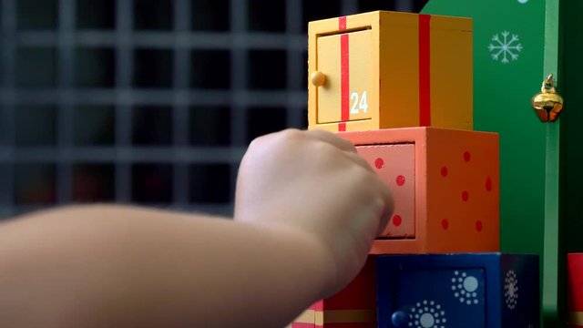 Close up of a little girl hand at Christmas Eve playing with an advent calendar, opening the doors unitl she finds crayons on the twenty fourth door
